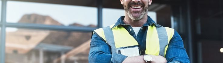 Man smiling while wearing a hard hat standing in front of a building