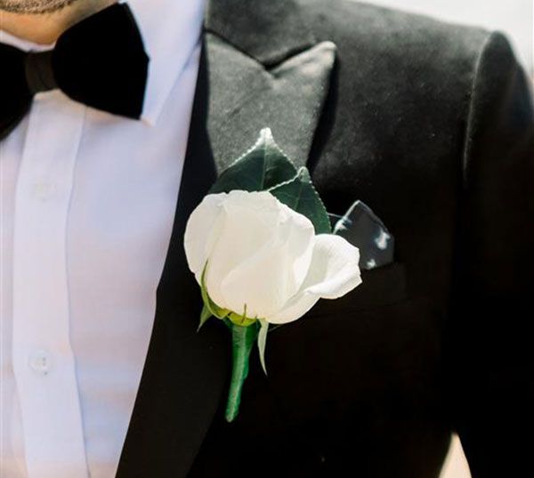 A close up shot of a groom with a white flower attached to the lapel of his black suit jacket